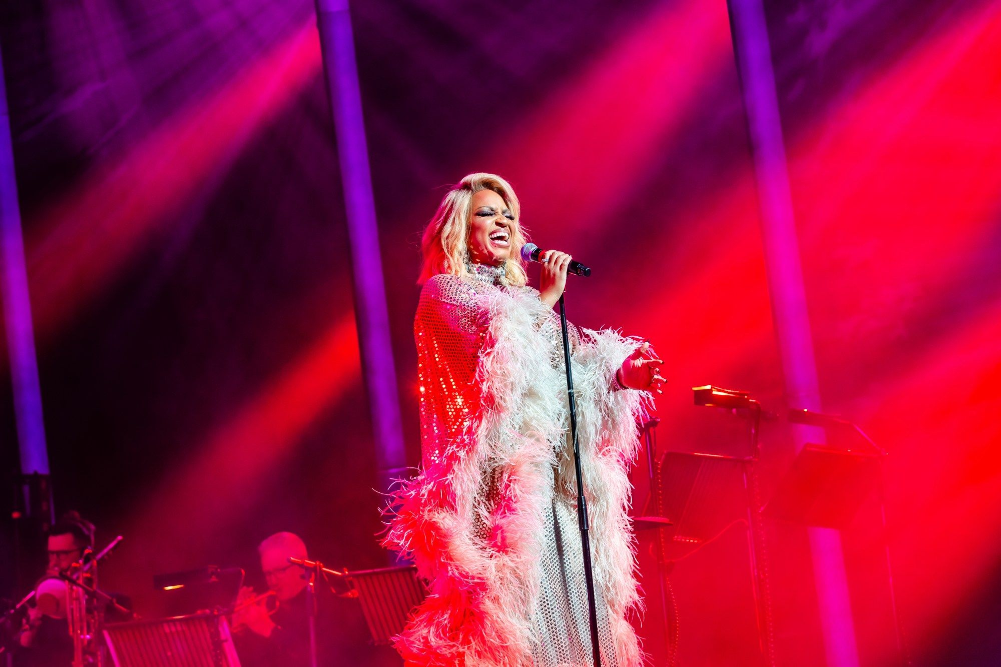 The stage glows red as Marisha Wallace sings with passion, her silver gown shimmering under the dramatic lighting.