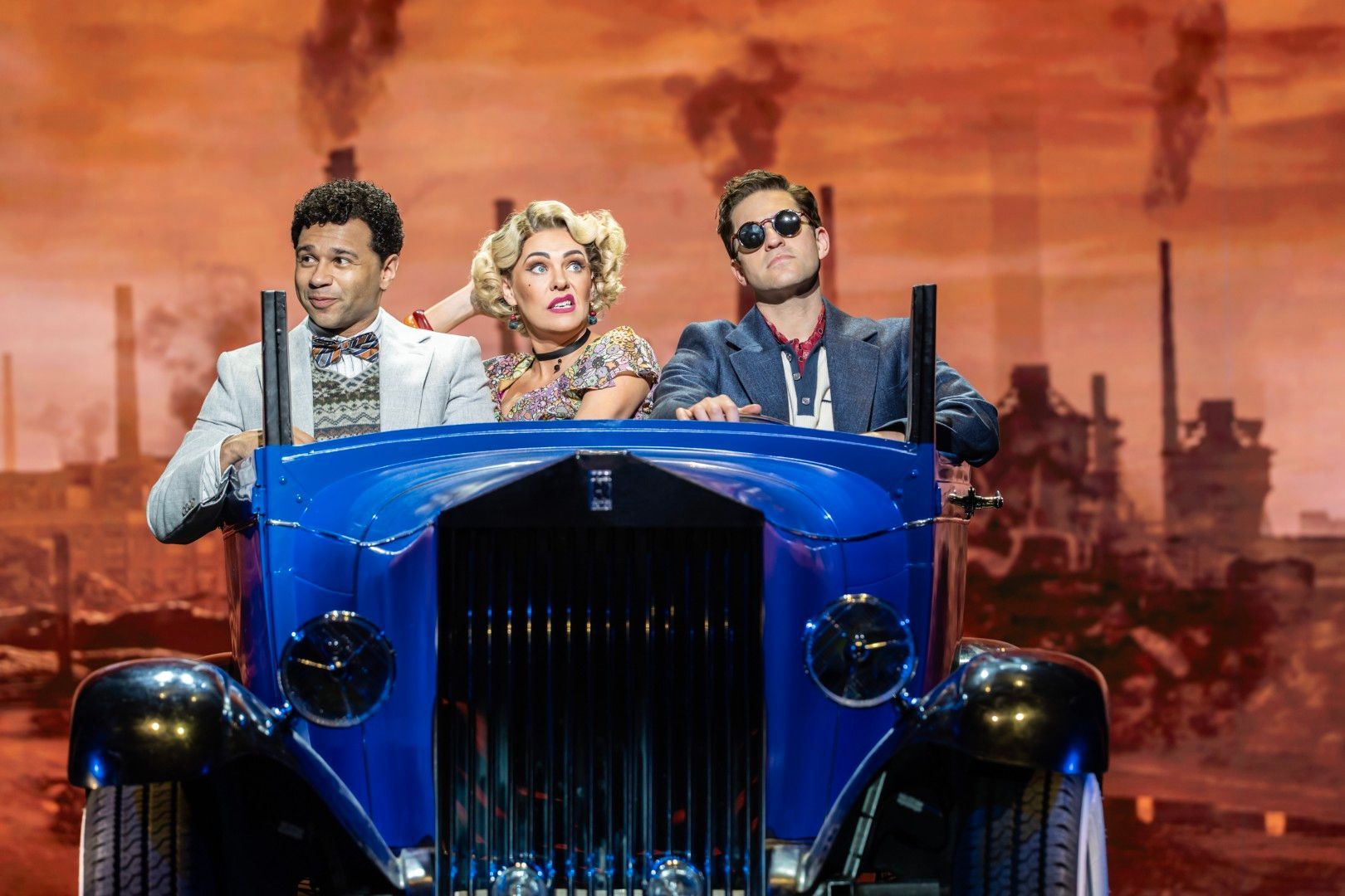 Corbin Bleu, Rachel Tucker, and Jon Robyns in a tense onstage moment, dressed in rich 1920s eveningwear, with dramatic lighting highlighting the tension.