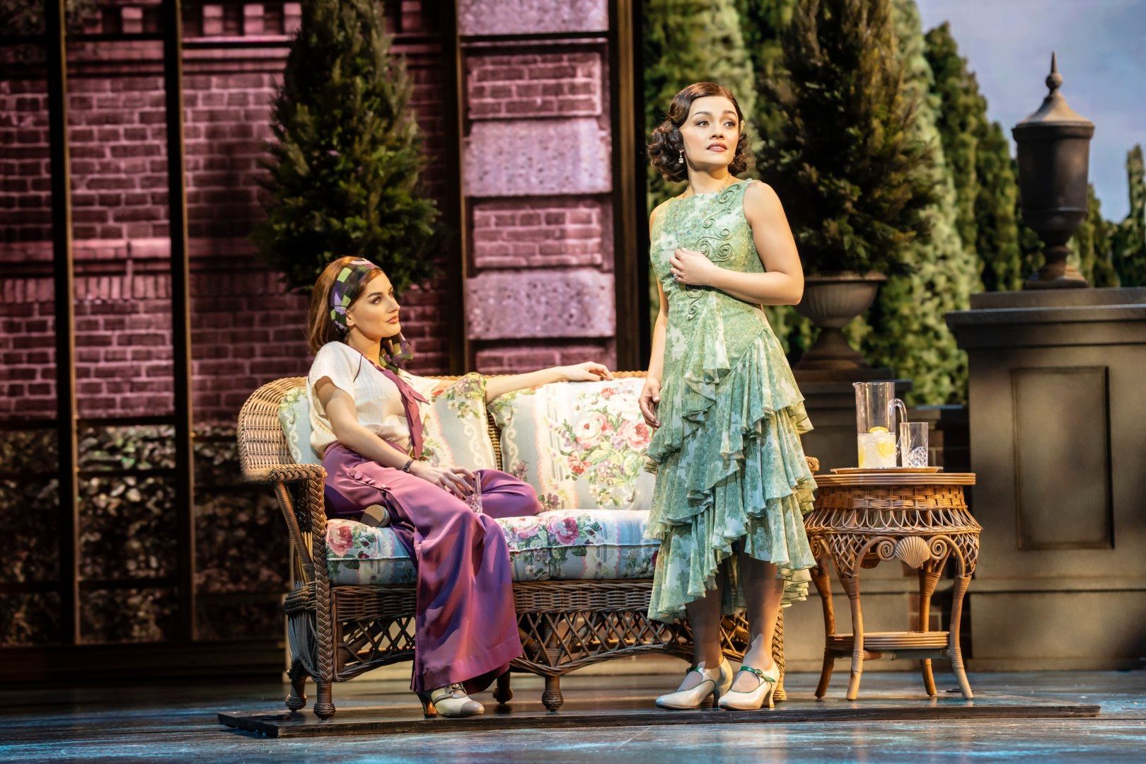 Frances Mayli McCann and Amber Davies, as Daisy and Jordan, sit close together in an elegant garden set, dressed in soft, glamorous pastels, lit in romantic tones.