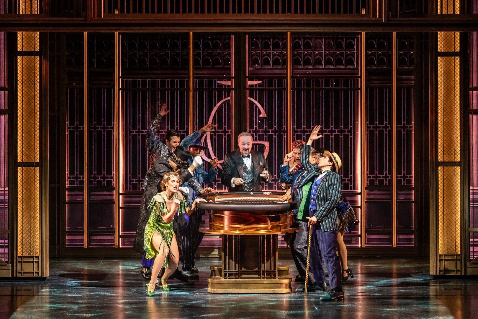John Owen-Jones, in character as Meyer Wolfsheim, leads the cast in a high-energy musical number, flanked by ensemble members in bold, stylised costumes.