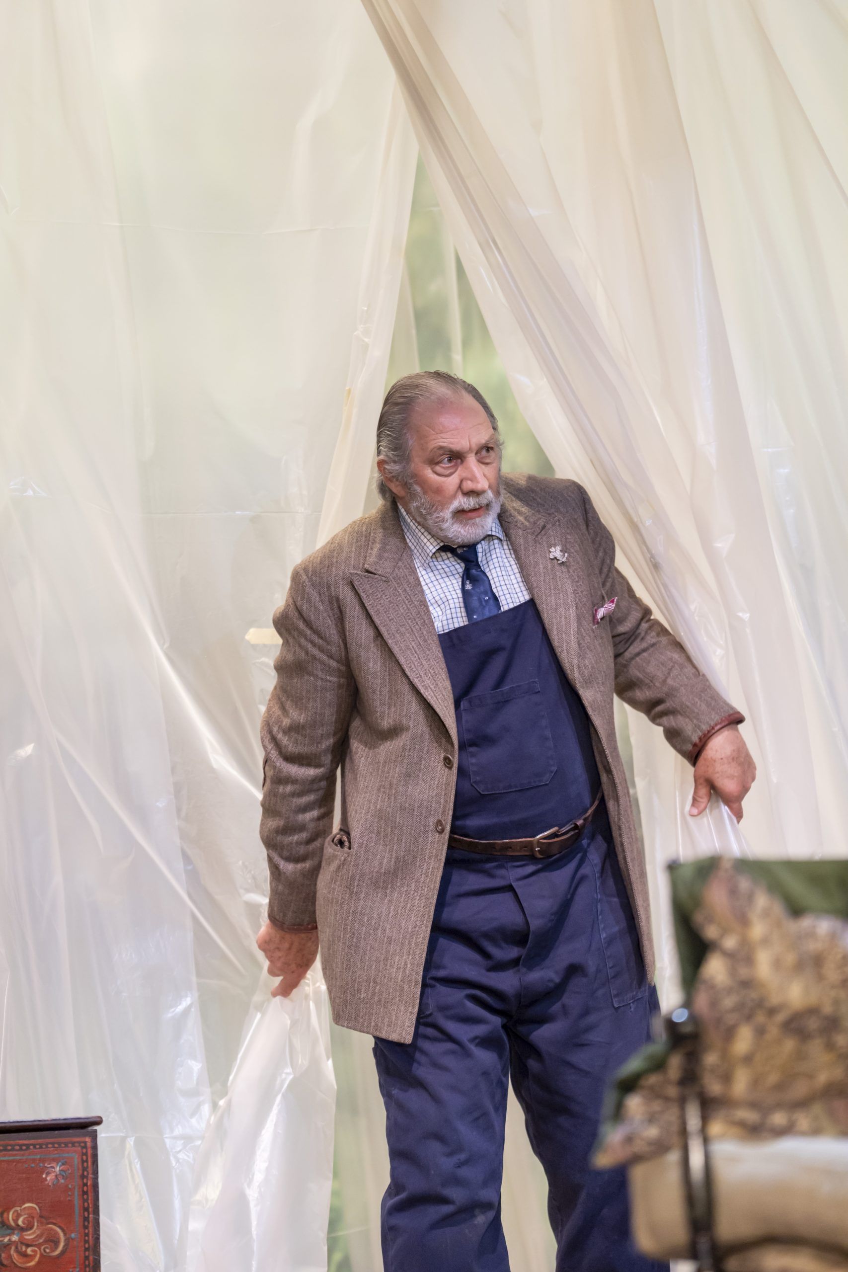 Richard Hope parts a plastic curtain and steps forward cautiously, dressed in a suit jacket over blue overalls.