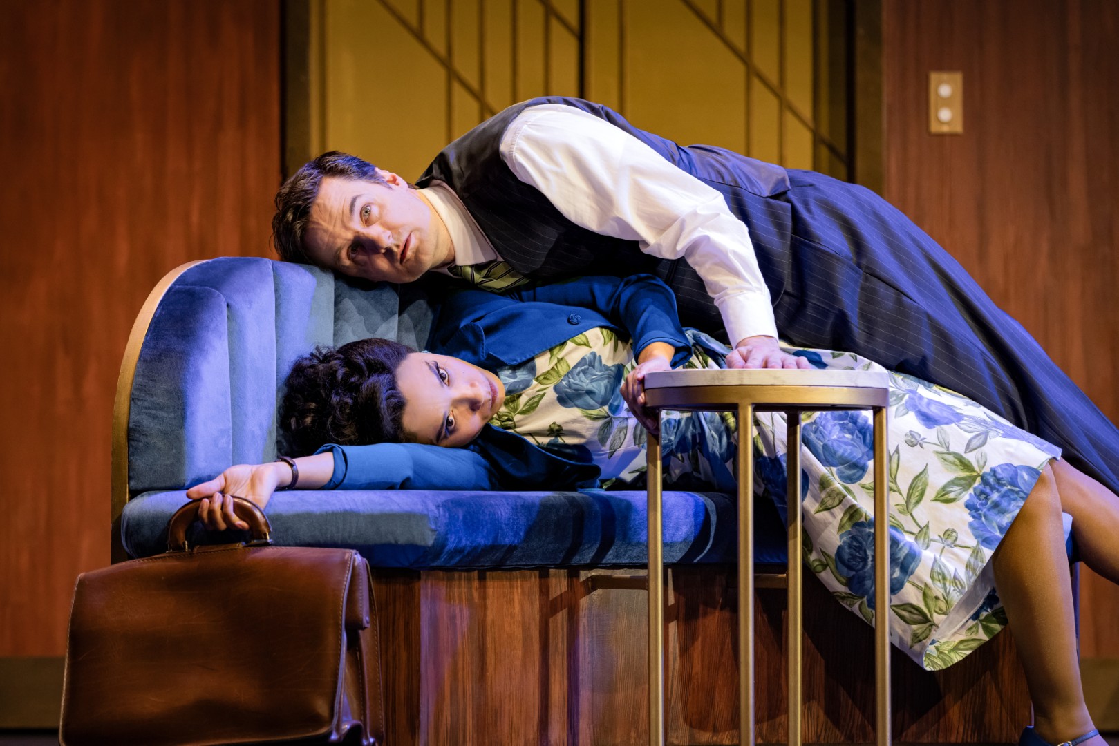 Adele James lies on a blue velvet hotel sofa while Henry Shields dramatically sprawls on top, both wide-eyed