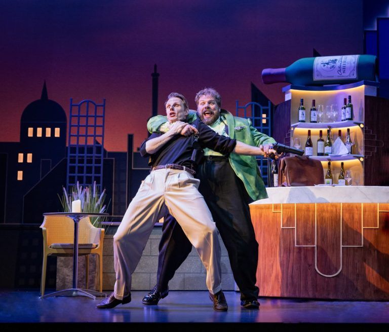 Henry Lewis grabs Dave Hearn in a headlock during a rooftop bar brawl, with a skyline backdrop and a giant bottle of Shiraz poised above the bar.