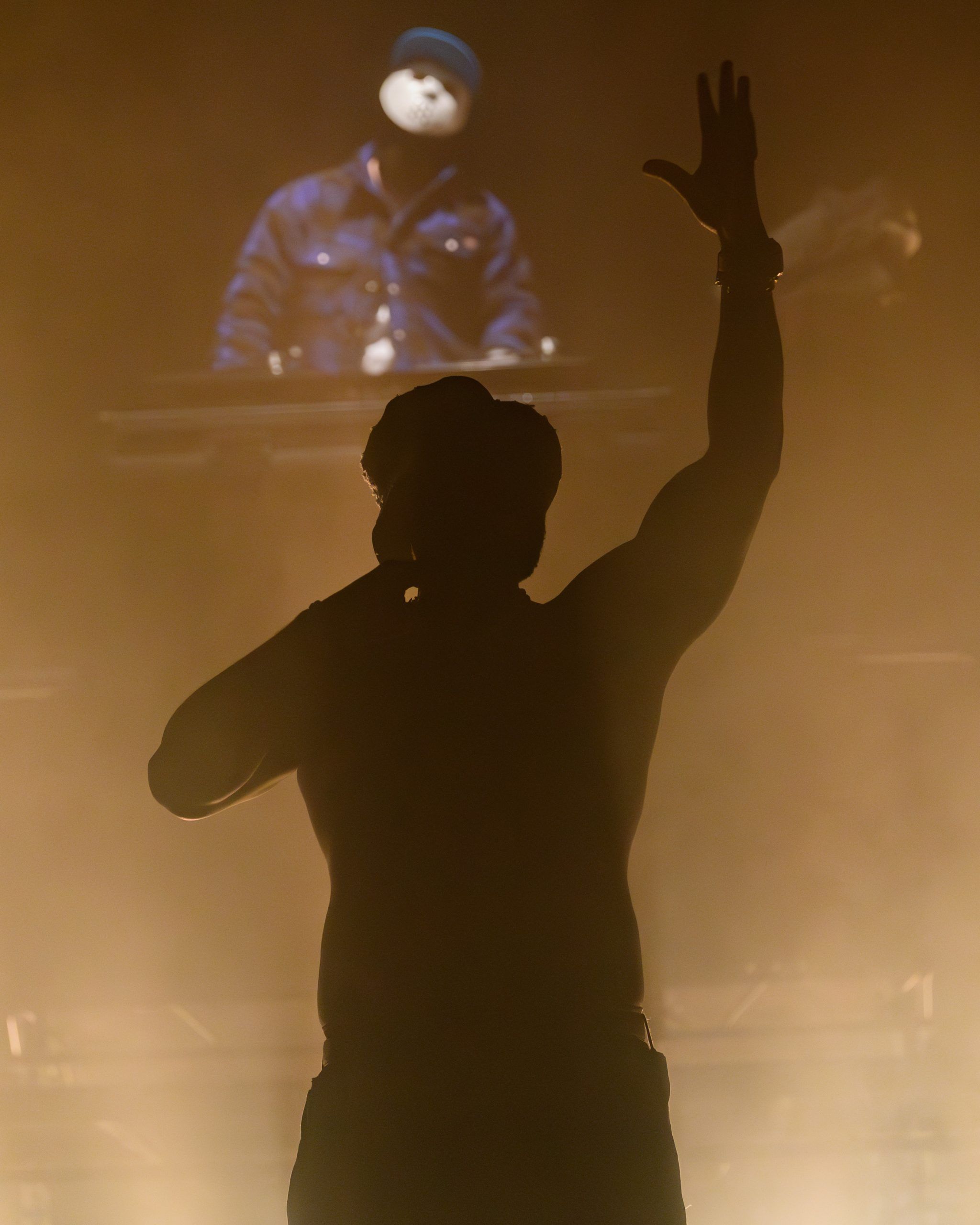 Clifford Samuel in camouflage jacket holding a mic, looking up into stage lights with an expressive face.