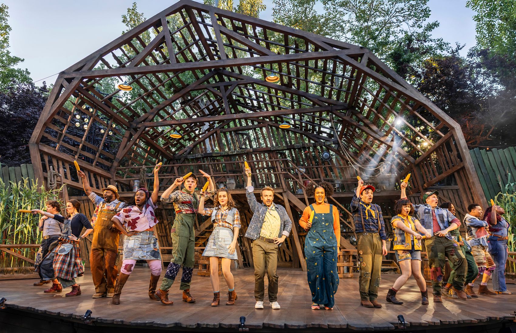 The ensemble of Shucked mid-dance number, each person in patchwork costumes holding a corn prop aloft.