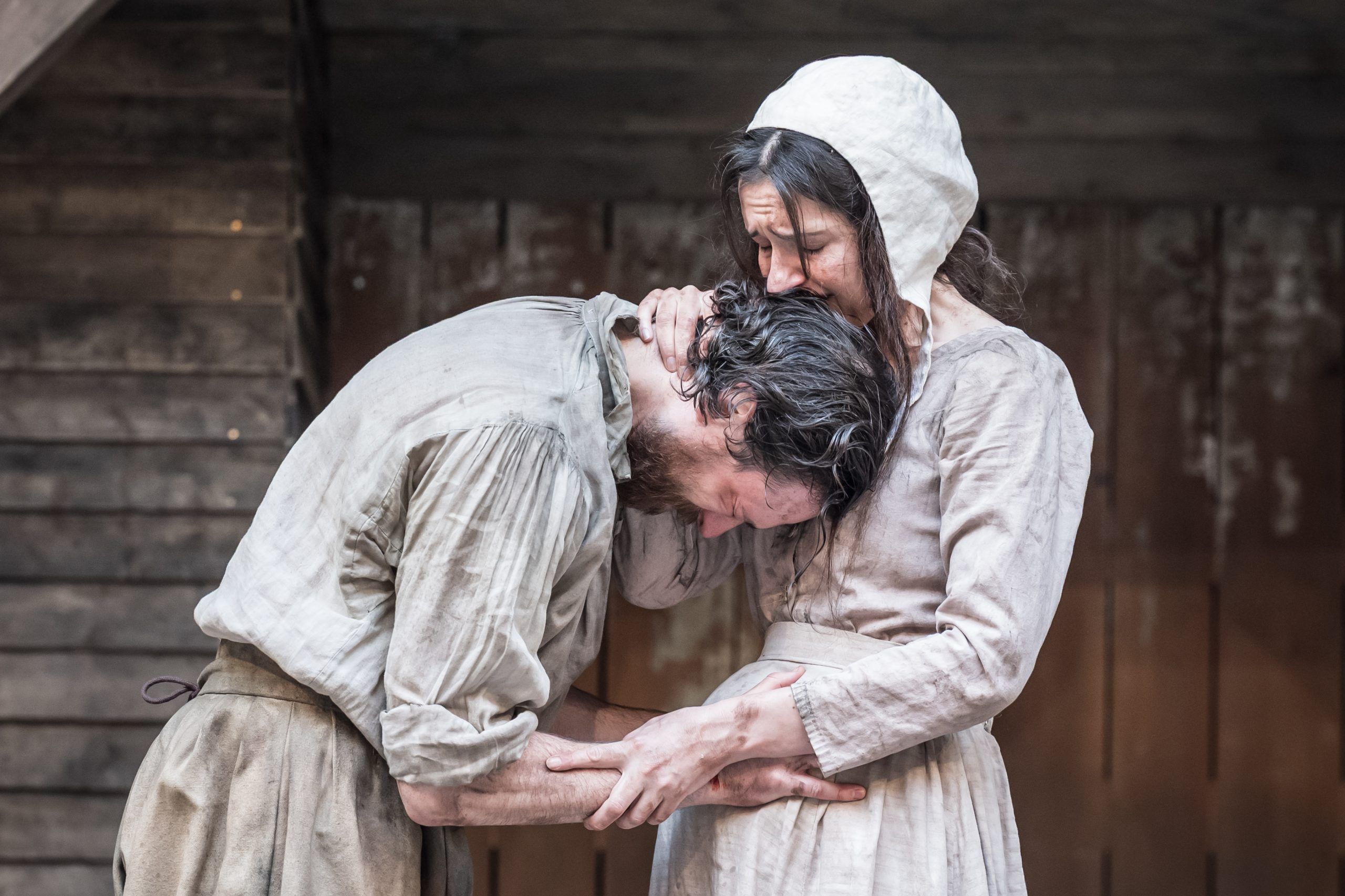 Gavin Drea clutches Phoebe Pryce in a raw, emotional embrace as John and Elizabeth Proctor, his head buried in her shoulder, her hand gripping his neck — a moment of tenderness and devastation.