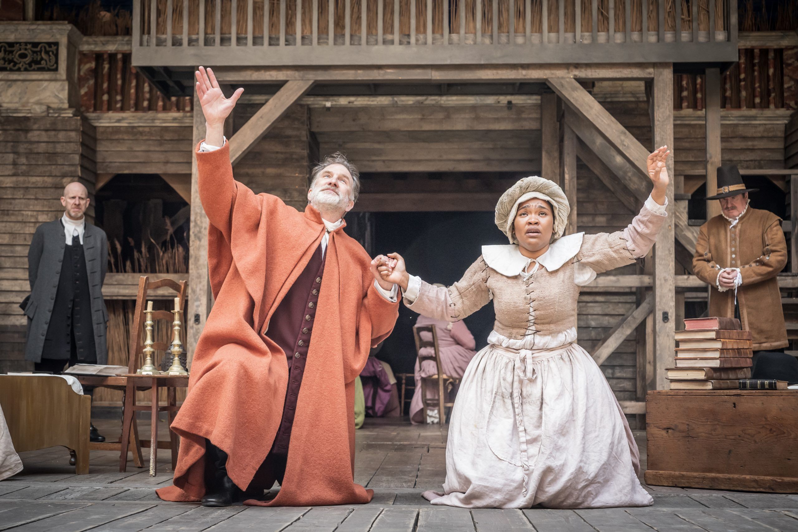 Jo Stone-Fewings raises his arms to the heavens in a fiery plea as Reverend Hale, while Sarah Merrifield as Tituba mirrors the gesture beside him, distraught and overwhelmed.