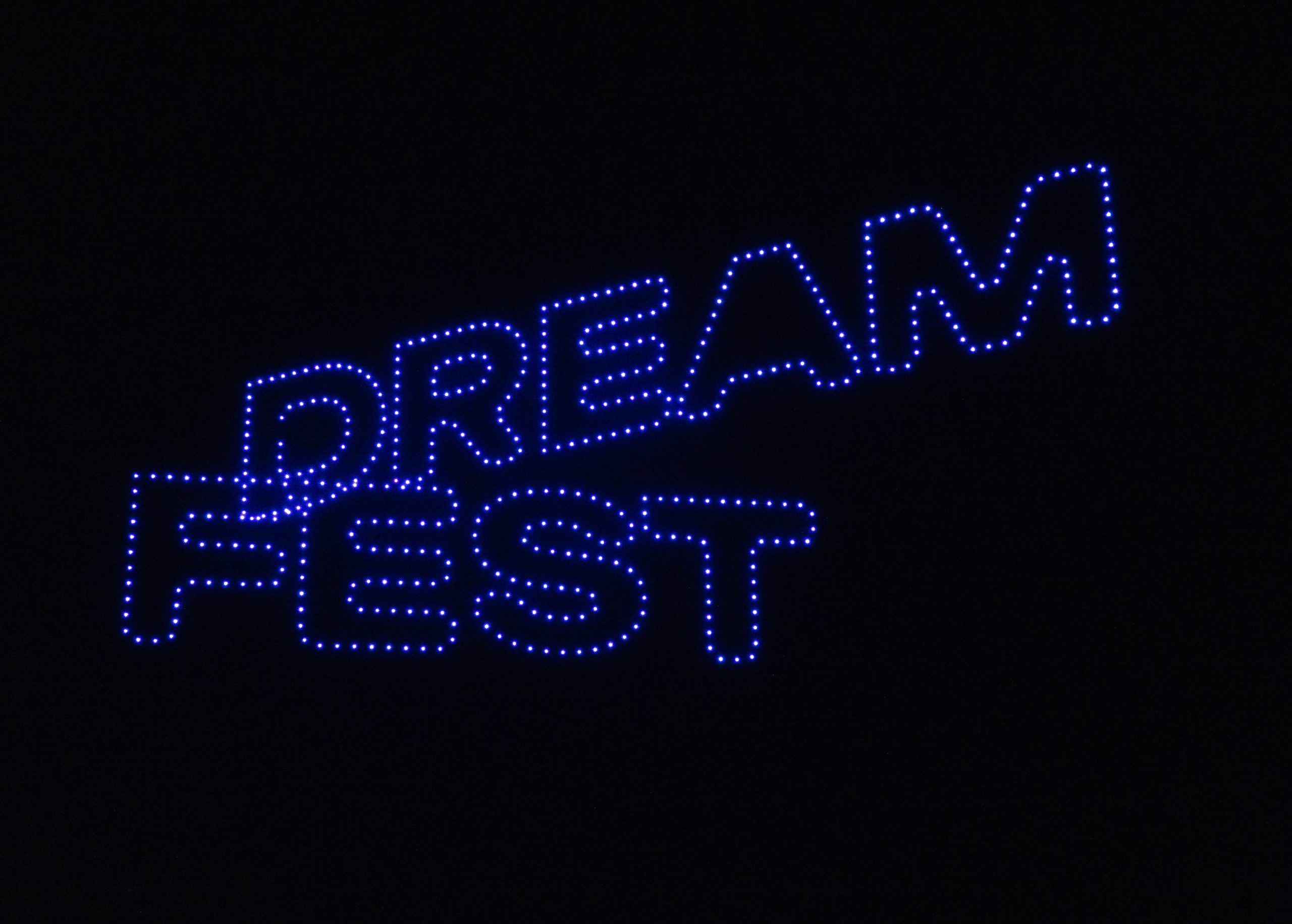 A close-up shot of the "DREAM FEST" logo displayed in bright blue, dotted LED drone lights against a dark night sky.