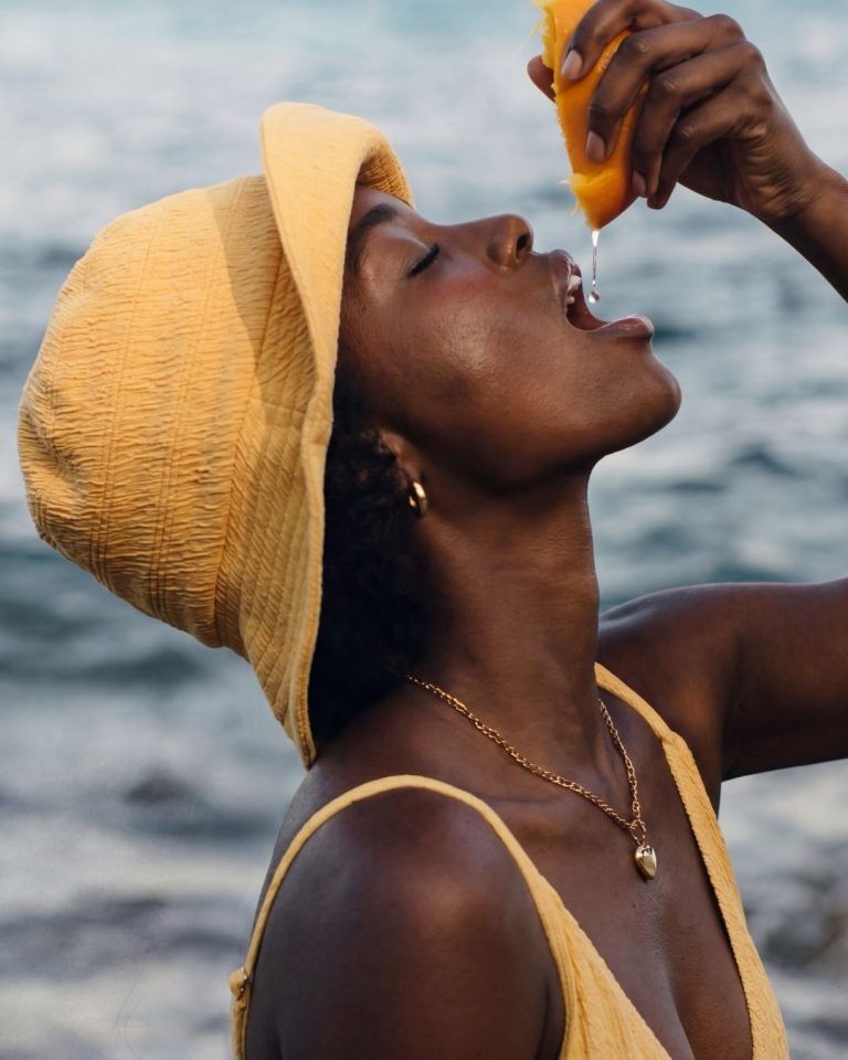 woman in yellow swimwear squeezing orange