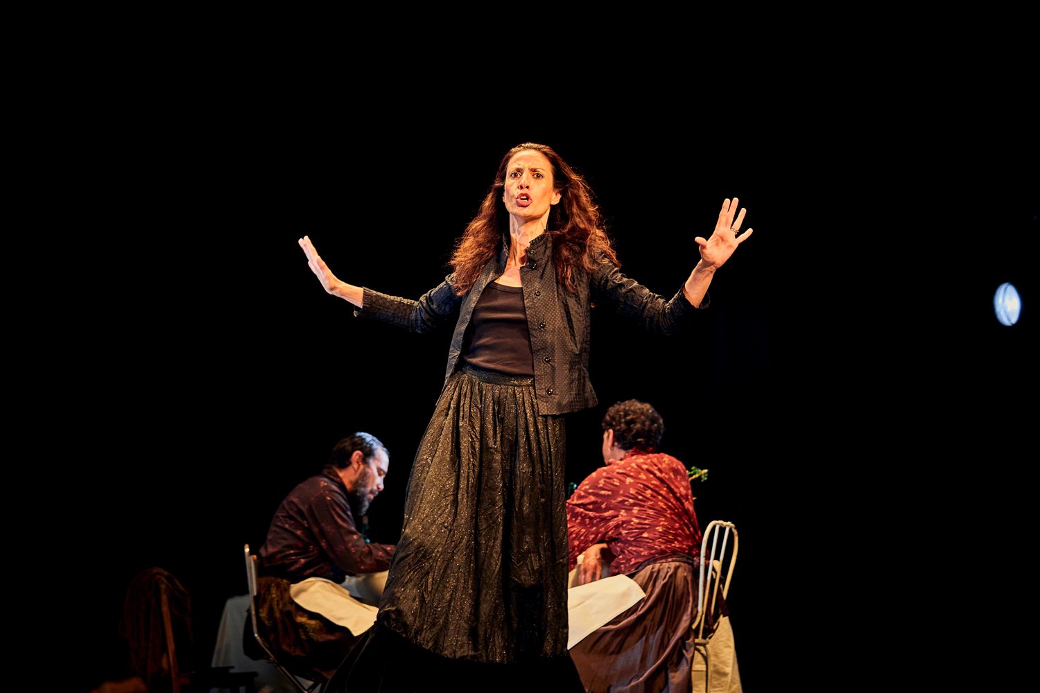 A performer raises both hands beside the dinner table in Catarina and the Beauty of Killing Fascists