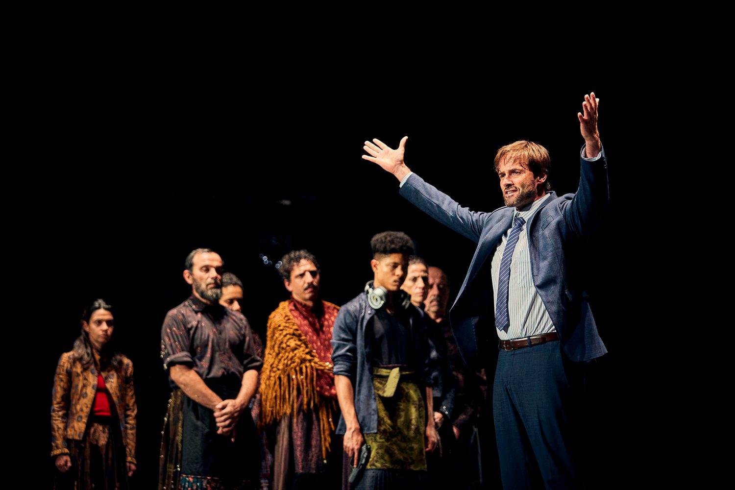 A suited speaker addresses the audience with the family behind him in Catarina and the Beauty of Killing Fascists