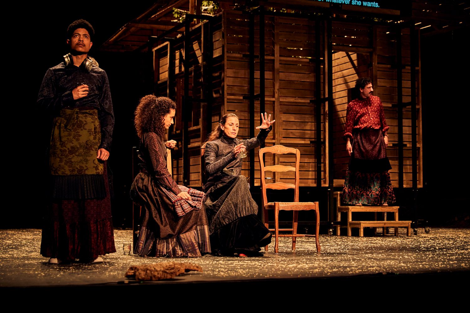 The family gathers around chairs on the wooden stage in Catarina and the Beauty of Killing Fascists